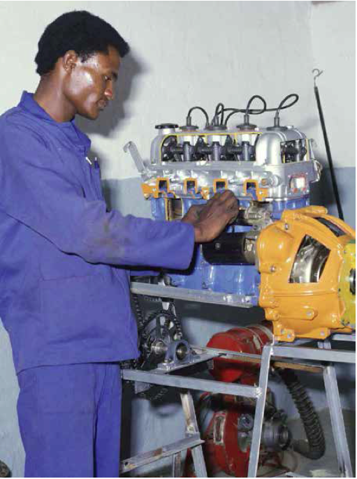 Artisan working on a car engine inside a workshop.
